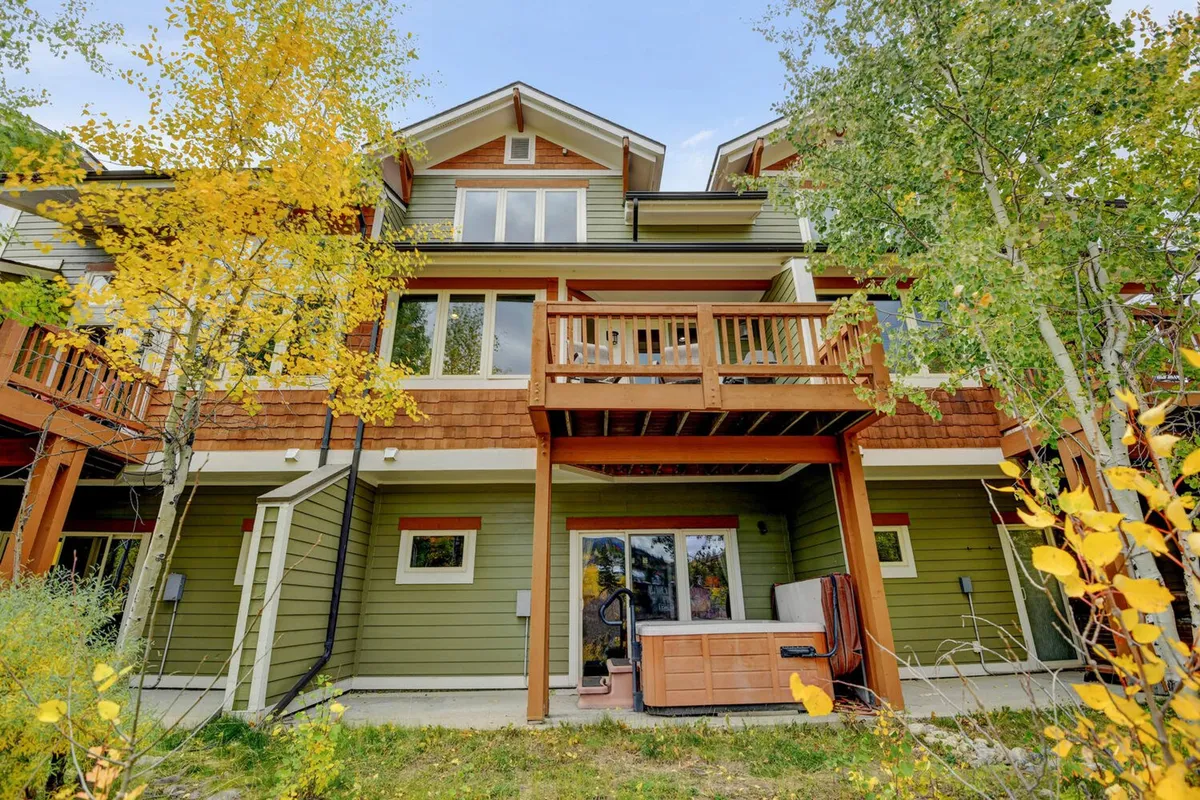 An inviting exterior scene featuring a villa's wooden balconies and a private hot tub set amidst lush surroundings and yellow autumn foliage. The setting offers views of nature and an appealing spot for relaxation.
