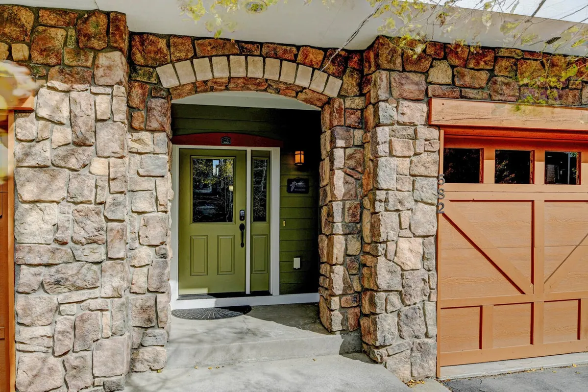 The exterior of the property featuring a welcoming stone archway, a green front door, and a wooden garage door. The entryway looks inviting and hints at the activities and adventures waiting just beyond, offering a sense of place and arrival at the home base for year-round exploration.