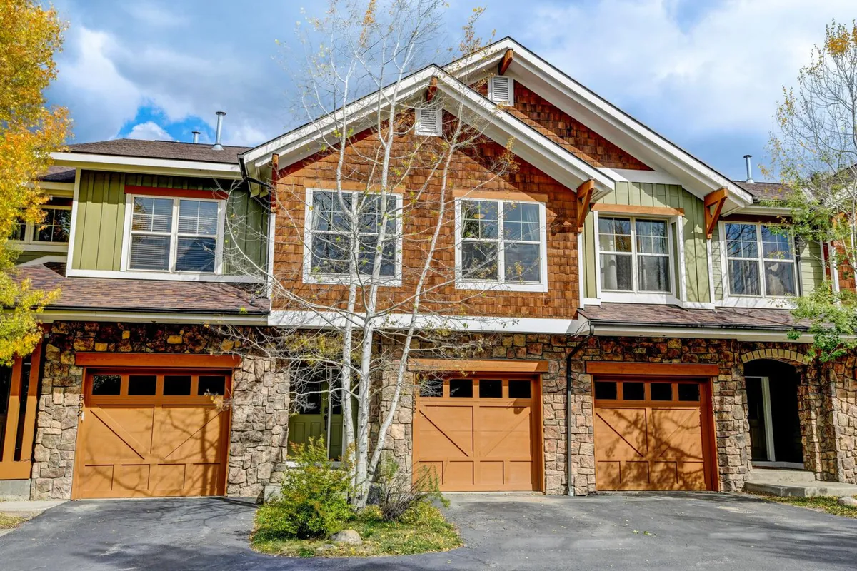 A brown stone villa facade with wooden garage doors, large windows, and a welcoming aspen tree in front. The inviting scene represents the neighborhood’s ambiance and the home’s immediate surroundings, suggesting easy strolls to local attractions.