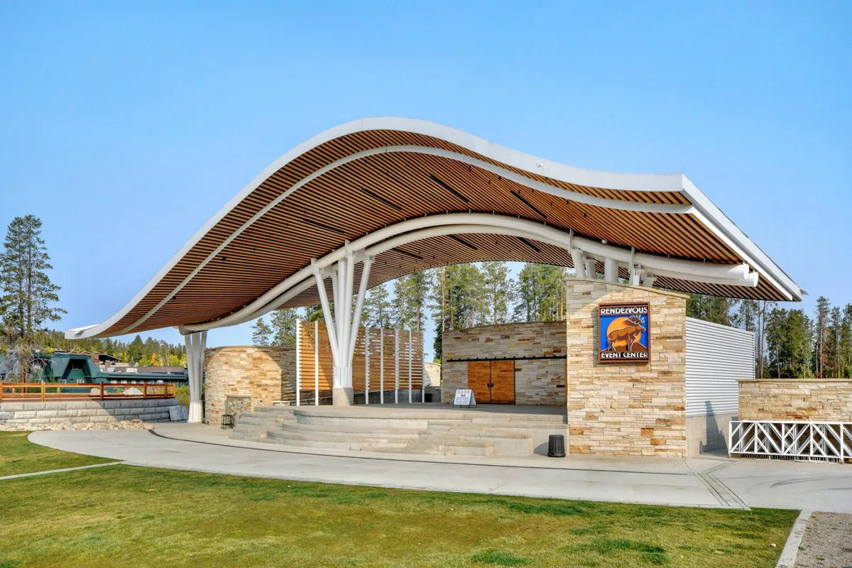 This image features the distinctive curved roof structure and stone walls of an amphitheater set amidst natural surroundings. The scene suggests a community gathering space ideal for live music, outdoor events, and festivals, with a festive and relaxed atmosphere.