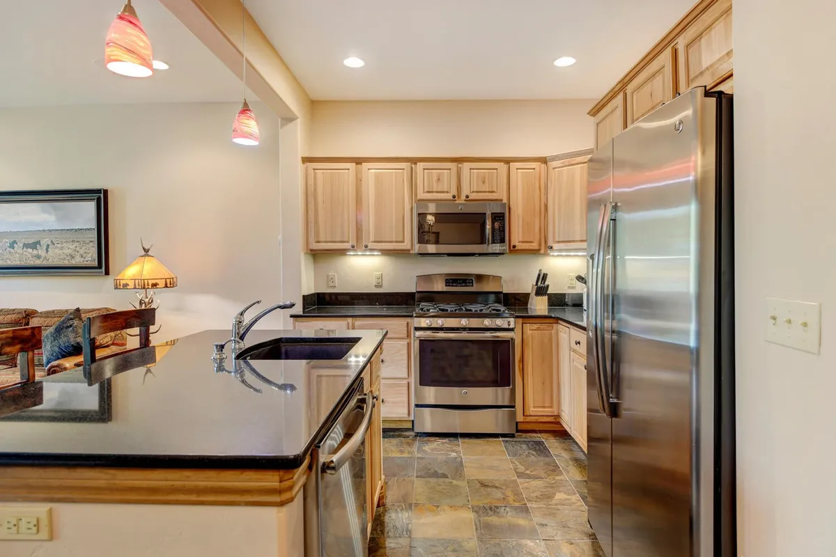 A beautifully designed kitchen with a striking granite countertop, stainless steel appliances, elegant pendant lighting, and warm wood cabinetry. The space is styled for meal preparation and group gatherings, suggesting a lively atmosphere for cooking classes or holiday meals.