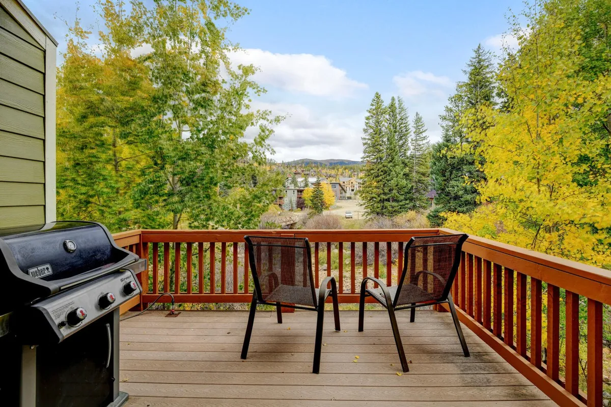A peaceful outdoor deck with a grill, comfortable chairs, and a railing overlooking the surrounding trees. The scene offers a secluded spot to relax and enjoy the fresh mountain air, with hints of scenic mountain views beyond the treeline.