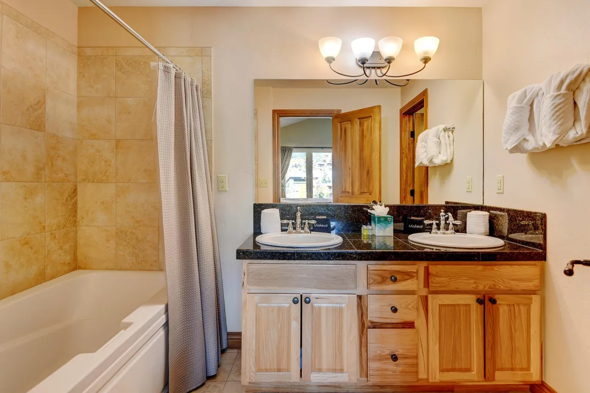 A serene bathroom scene featuring a spacious double sink vanity, a bathtub with a shower curtain, and a large mirror. The space feels spa-like and calming, ideal for personal grooming and relaxation.